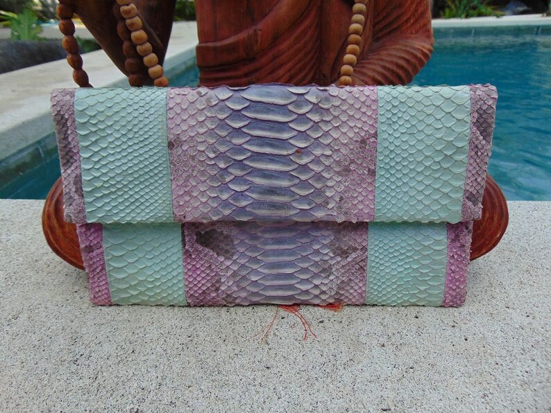 Pu&ograve; includere: Una pochette in pelle di serpente blu chiaro e viola con chiusura a lembo.