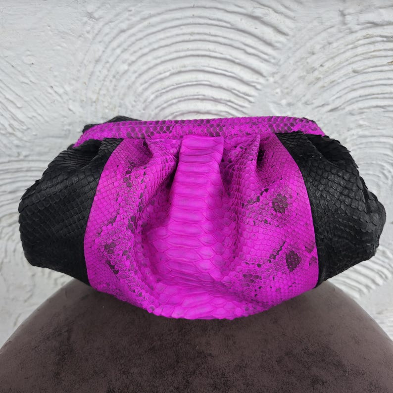 Peut inclure: Une pochette de soir&eacute;e en cuir de serpent rose vif et noir. La pochette est en cuir de serpent v&eacute;ritable et pr&eacute;sente un design textur&eacute; unique.