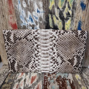 Pu&ograve; includere: Un primo piano di una pochette in pelle di serpente bianca e marrone. La pochette &egrave; realizzata in vera pelle di pitone e ha una lucentezza discreta.