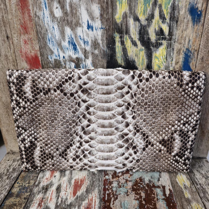 Pu&ograve; includere: Un primo piano di una pochette in pelle di serpente bianca e marrone. La pochette &egrave; realizzata in vera pelle di pitone e ha una lucentezza discreta.