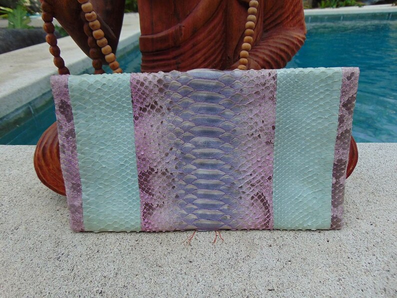 Pu&ograve; includere: Una pochette in pelle di serpente blu chiaro e rosa con un design a righe.