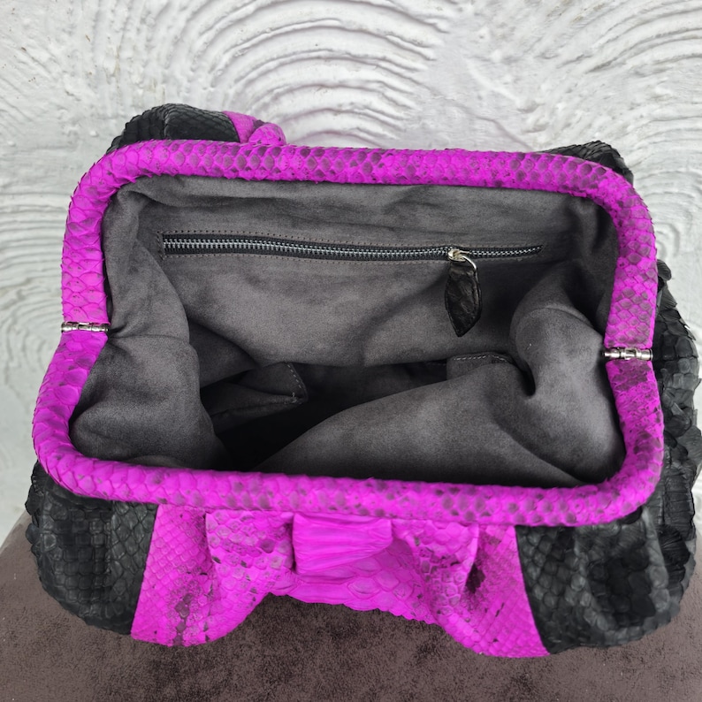 Peut inclure: Un sac &agrave; main en cuir de serpent noir et magenta avec une fermeture &agrave; glissi&egrave;re. Le sac est ouvert et l'int&eacute;rieur est doubl&eacute; d'un tissu gris fonc&eacute;.