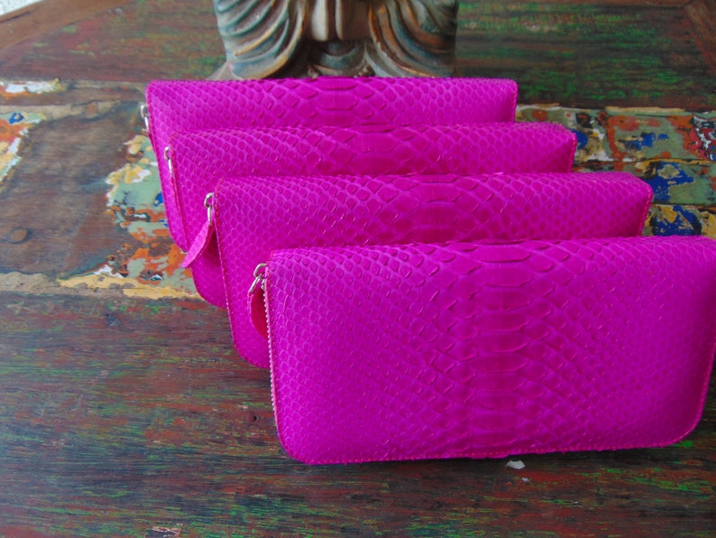 K&ouml;nnte beinhalten: Vier leuchtend pinkfarbene Geldb&ouml;rsen mit Schlangenhautmuster. Die Geldb&ouml;rsen sind &uuml;bereinander gestapelt.