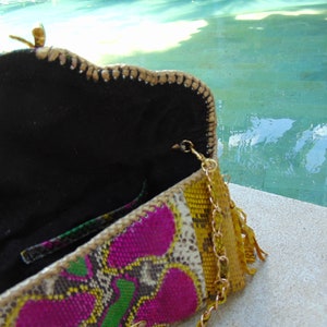 May include: A colourful clutch purse with a gold chain strap and a tassel. The purse is made from a variety of materials, including snakeskin, leather, and fabric. The purse is open and the inside is lined with black fabric.