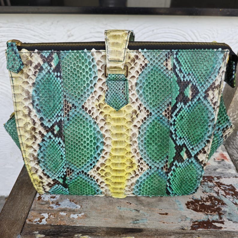 K&ouml;nnte beinhalten: Eine gr&uuml;ne, gelbe und blaue Schlangenleder-Handtasche mit einem goldenen Rei&szlig;verschluss und einem goldenen Verschluss.
