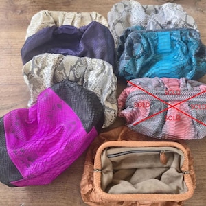 May include: A collection of eight clutch bags in various colors and textures, including snakeskin patterns in beige, gray, and blue, a solid purple bag, a bright pink and black bag, and an open tan bag with a beige interior lining.