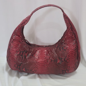 May include: A red snakeskin hobo bag with a curved shape and a single shoulder strap. The bag features a zipper closure and a textured surface, showcasing the natural pattern of the snakeskin.