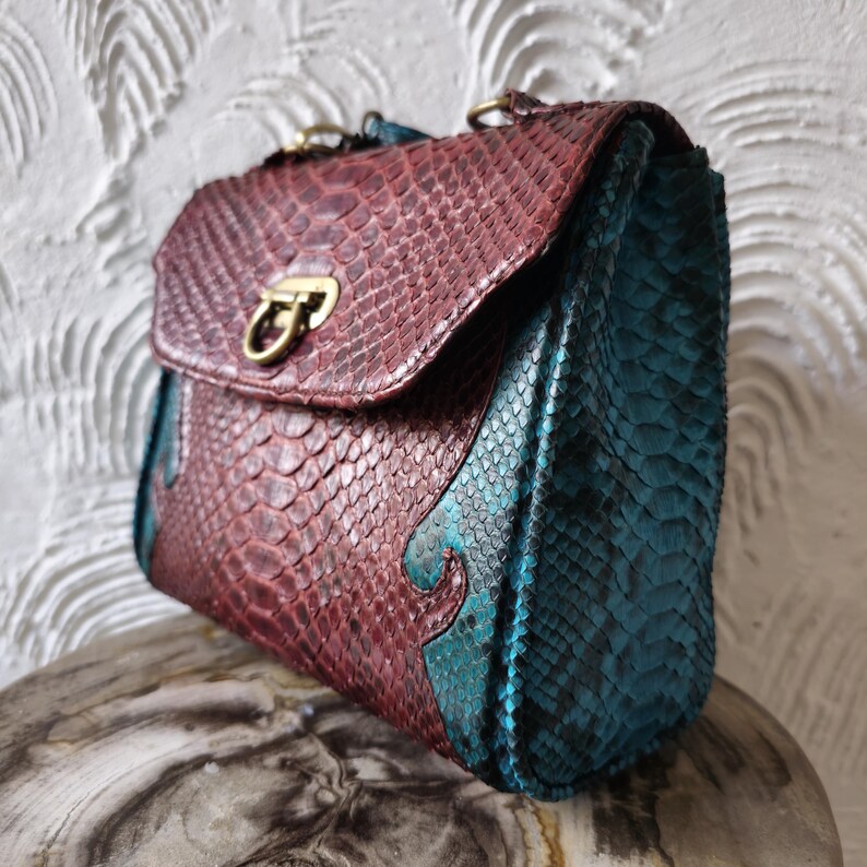 May include: A small, burgundy and teal snakeskin handbag with a brass clasp.