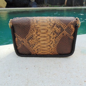 Peut inclure: Une pochette en cuir de serpent brun et beige avec une bordure noire et une cha&icirc;ne dor&eacute;e.