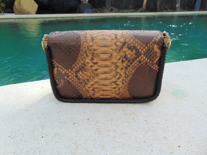 Peut inclure: Une pochette en cuir de serpent brun et beige avec une bordure noire et une cha&icirc;ne dor&eacute;e.