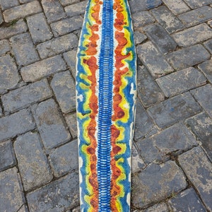 May include: A long, colourful snake skin with a blue, yellow and orange pattern. The skin is laid out flat on a grey brick surface.