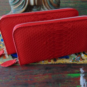 May include: Two red leather wallets with a snakeskin pattern and silver zips. The wallets have a small leather tassel on each zip pull.