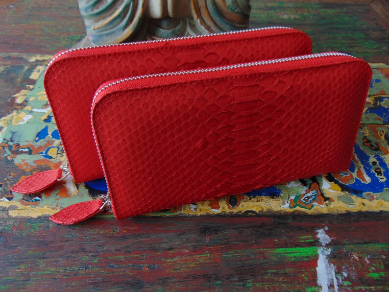 May include: Two red leather wallets with a snakeskin pattern and silver zips. The wallets have a small leather tassel on each zip pull.