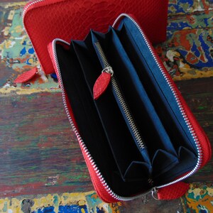 May include: A red leather zipped wallet with a black interior and multiple card slots. The wallet is open and the zipper is visible.
