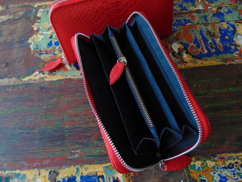 May include: A red leather zipped wallet with a black interior and multiple card slots. The wallet is open and the zipper is visible.