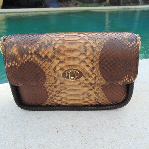Peut inclure: Un petit sac &agrave; main en cuir de serpent brun et beige avec une fermeture dor&eacute;e et une bandouli&egrave;re en cha&icirc;ne noire.