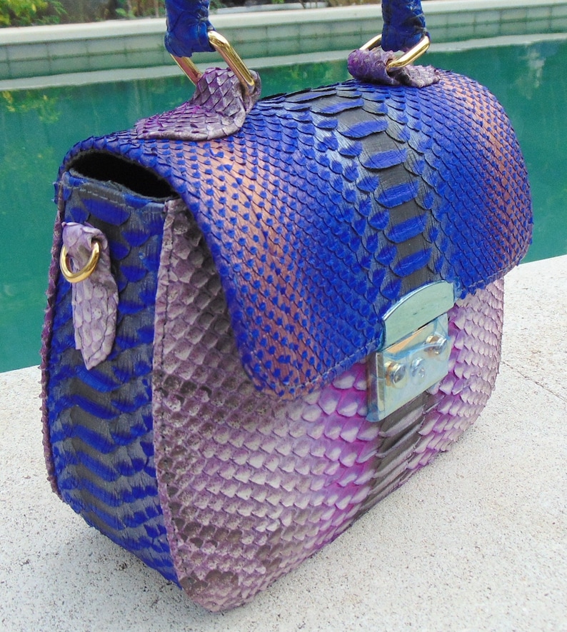 May include: A small, blue and purple snakeskin handbag with a gold clasp and a top handle.
