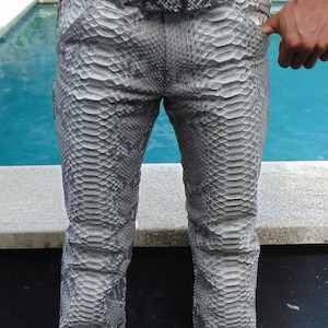 K&ouml;nnte beinhalten: Grau-wei&szlig; gemusterte Hose mit Schlangenleder-Optik und passendem G&uuml;rtel. Die Hose hat ein klassisches F&uuml;nf-Taschen-Design und einen geraden Beinverlauf. Der G&uuml;rtel hat eine silberne Schnalle. Die Hose besteht aus einem Material, das die Textur von Schlangenleder nachahmt.