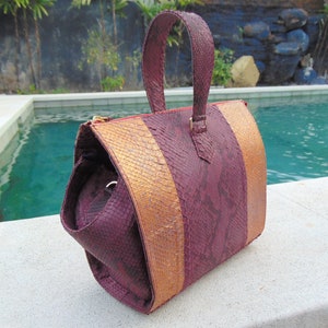 May include: A burgundy and gold snakeskin handbag with a top handle. The bag has a textured snakeskin pattern and a gold zipper.
