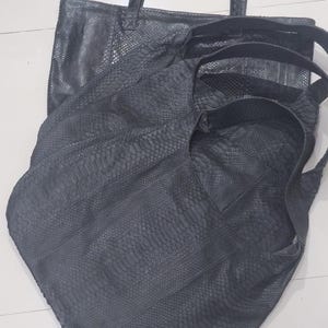 May include: A collection of three dark gray tote bags featuring a textured snakeskin pattern. Each bag is constructed with two shoulder straps and a spacious main compartment, showcasing a consistent scale-like surface design across all items.