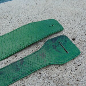 Könnte beinhalten: Zwei grüne Ledergitarrengurte mit Schlangenhautmuster. Die Gurte sind an den Rändern zusammengenäht.