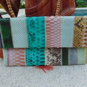 Op de afbeelding: Een veelkleurige clutch van slangenleer met een kwast. De clutch is gemaakt van verschillende soorten slangenleer, waaronder groen, blauw, roze en bruin.