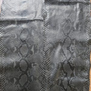 May include: Two pieces of dark gray snakeskin leather with a scale pattern. The leather has a textured surface and a natural, irregular edge. The pattern includes darker gray markings, creating a realistic reptile skin appearance.