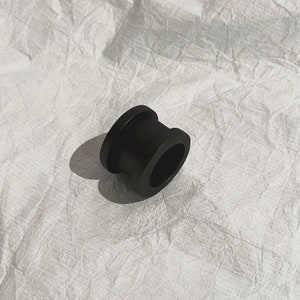 K&ouml;nnte beinhalten: Ein schwarzer Gummiring mit einer glatten, abgerundeten Oberfl&auml;che. Der Ring ist so konzipiert, dass er um ein Rohr oder ein anderes zylindrisches Objekt passt.