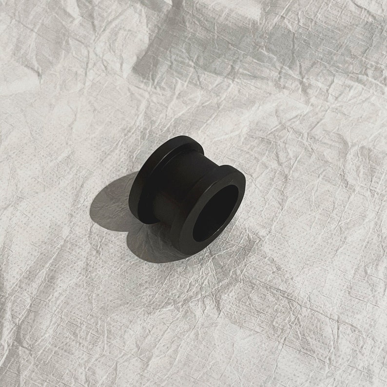 K&ouml;nnte beinhalten: Ein schwarzer Gummiring mit einer glatten, abgerundeten Oberfl&auml;che. Der Ring ist so konzipiert, dass er um ein Rohr oder ein anderes zylindrisches Objekt passt.