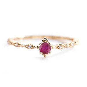 May include: A delicate gold ring with a ruby gemstone surrounded by small diamonds. The band is adorned with a delicate beaded design.