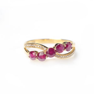以下が含まれることがあります： 曲線的なデザインに配置された、鮮やかな赤い宝石、おそらくルビーが連なったゴールドリング。 バンドは小さな輝くアクセントストーンで飾られ、豪華でエレガントな外観を作り出しています。 リングは白い背景に表示されています。