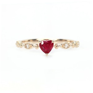 May include: A delicate gold ring with a heart-shaped ruby gemstone and small diamonds set in a delicate filigree design.
