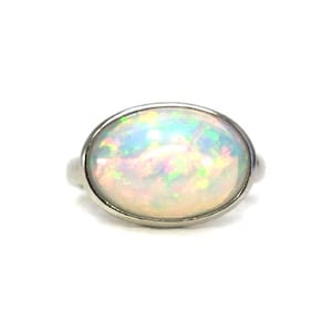 Puede incluir: Un anillo de plata con una piedra preciosa de ópalo blanco. El ópalo presenta un arcoíris de colores, incluyendo verde, rosa y azul.