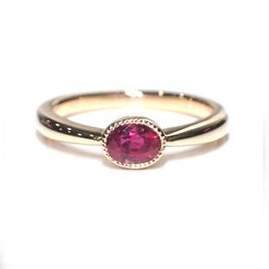 Può includere: Un delicato anello a fascia d'oro con una piccola pietra preziosa di rubino di forma ovale incastonata al centro.