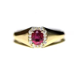May include: A gold ring with a red oval ruby gemstone surrounded by a halo of smaller diamonds.