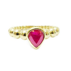 Könnte beinhalten: Ein goldener Ring mit einer Perlenkette und einem tropfenförmigen Rubin.