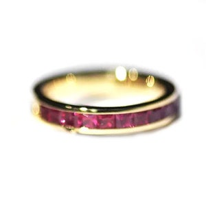 Puede incluir: Un anillo de banda de oro con una fila de piedras de rubí rojo engastadas en la banda.