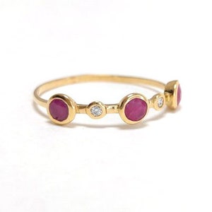 Puede incluir: Un anillo de oro con tres piedras de rub&iacute; rojo y una piedra de diamante blanco. Las piedras est&aacute;n engastadas en un engaste de bisel y est&aacute;n rodeadas por una fina banda de oro.