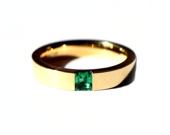 Puede incluir: Un anillo de banda de oro con una piedra preciosa cuadrada verde esmeralda engastada en el centro.