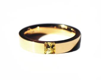 Puede incluir: Un anillo de banda de oro con una piedra preciosa amarilla cuadrada en el centro.
