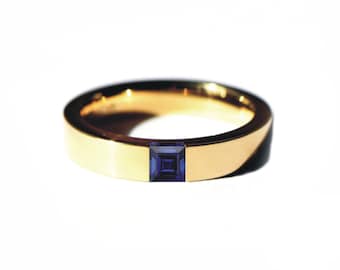 May include: A gold band ring with a square-shaped blue sapphire gemstone set in the center.