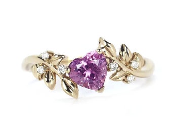 May include: A gold ring with a heart-shaped pink sapphire and diamond accents. The ring features a delicate leaf design.