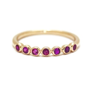 May include: A gold band ring with seven small, round, bezel-set ruby stones.