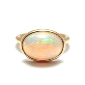 May include: A gold ring featuring a large oval opal gemstone. The opal is a milky white colour with flashes of green, blue, and pink.