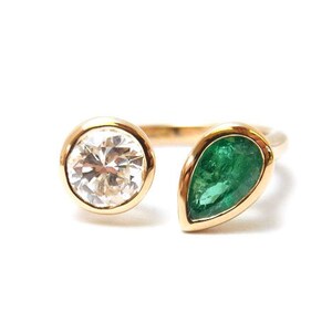 May include: A gold ring with a round white gemstone and a pear-shaped green gemstone.