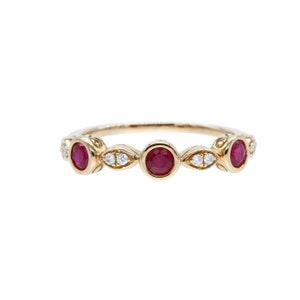 May include: A gold band ring with three red ruby stones and small diamonds set in the band.