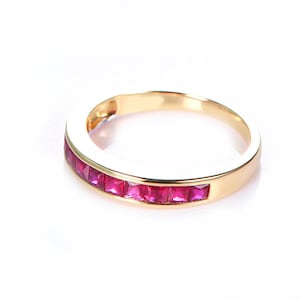 Puede incluir: Un anillo de banda de oro con una fila de piedras de rubí rojo.