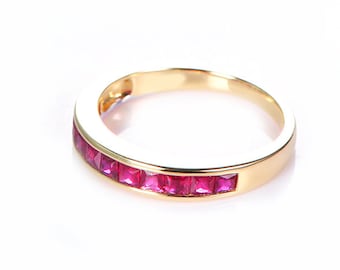 Puede incluir: Un anillo de banda de oro con una fila de piedras de rubí rojo.