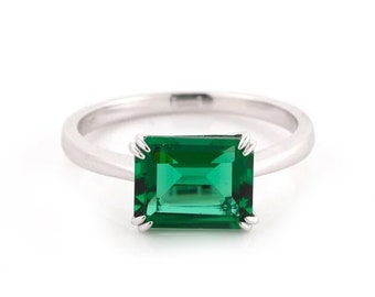 May include: A silver ring with a large emerald green gemstone set in a square shape.