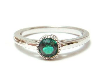 May include: A silver ring with a green gemstone set in a bezel setting. The ring has a delicate, textured band.